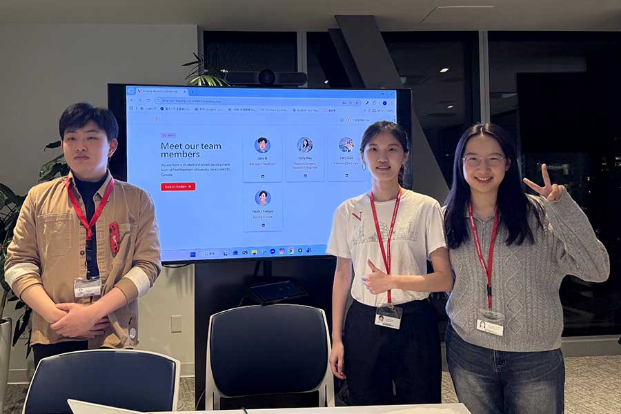 Three Khoury students stand in front of a large screen displaying team members who worked on a website to connect current Khoury students with Khoury alumni working in the students’ desired career field