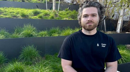 Ben Senescu sits in a landscape with tiers of green plants in the background