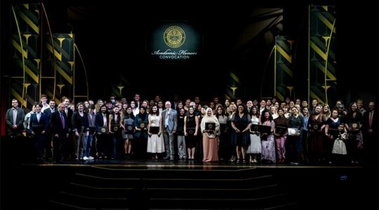 Dozens of Northeastern graduates pose for a photo with Northeastern President Joseph Aoun on a stage