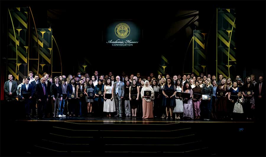 Dozens of Northeastern graduates pose for a photo with Northeastern President Joseph Aoun on a stage