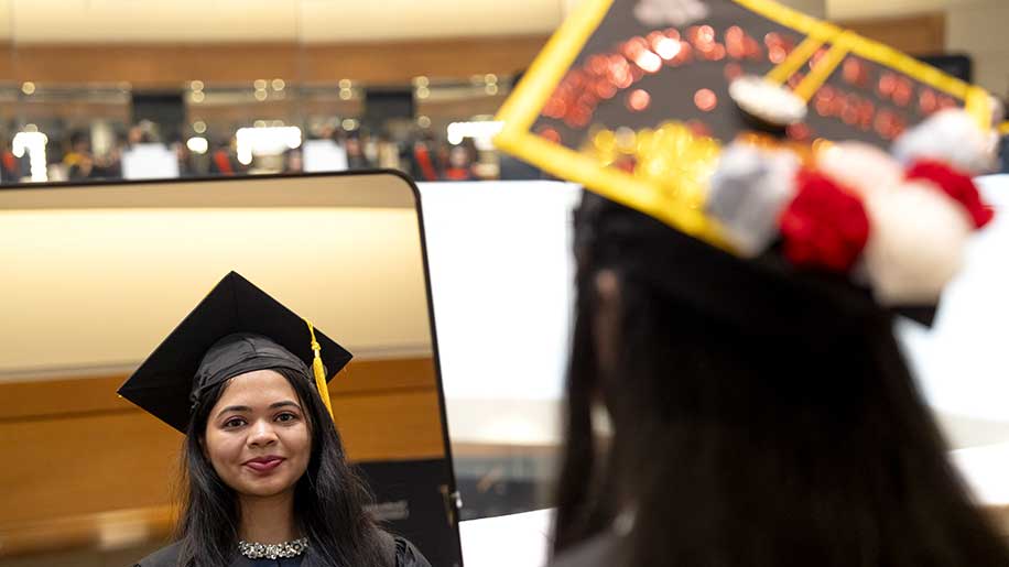 New Khoury graduate Mansi Modi looks in a mirror before the ceremony