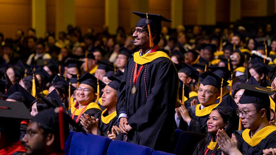 New Khoury graduate Kalhar Pandya stands up in the audience during the graduation ceremony