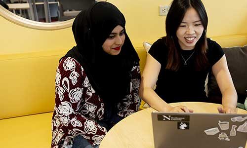 Aisha Abdur Rahim and Yi Zhang view a laptop while sitting at a table at a cafe