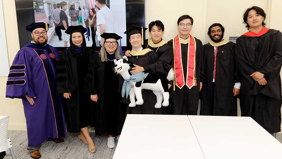 Northeastern University Miami faculty post for a photo with Khoury's graduating students, one of whom is holding a large stuffed husky