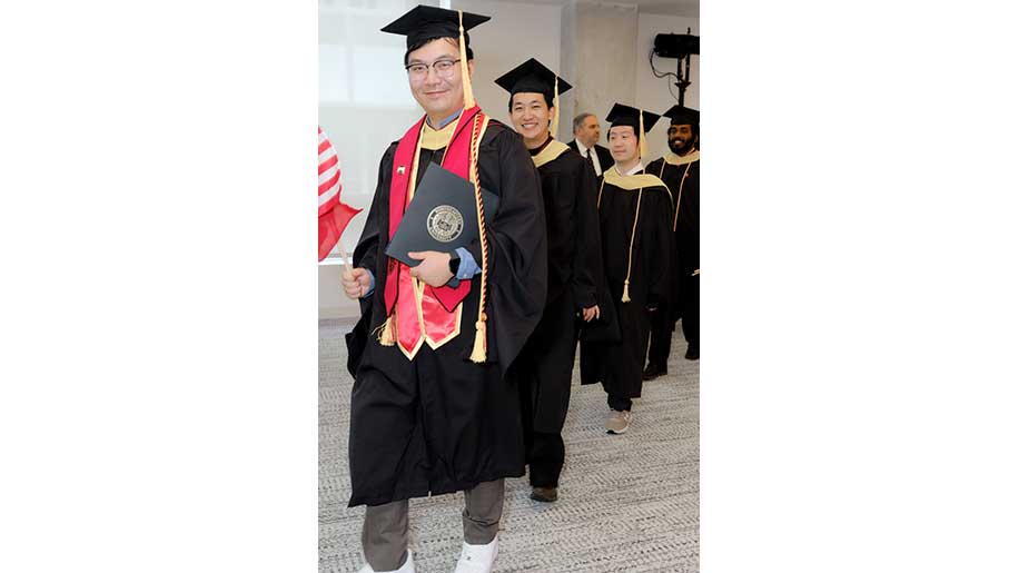 Khoury graduates walk in a single-file line after receiving their diplomas at Northeastern University Miami's commencement celebration