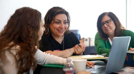 A Khoury student and two local business leaders view a laptop while sitting at a large table