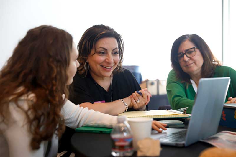 A Khoury student and two local business leaders view a laptop while sitting at a large table