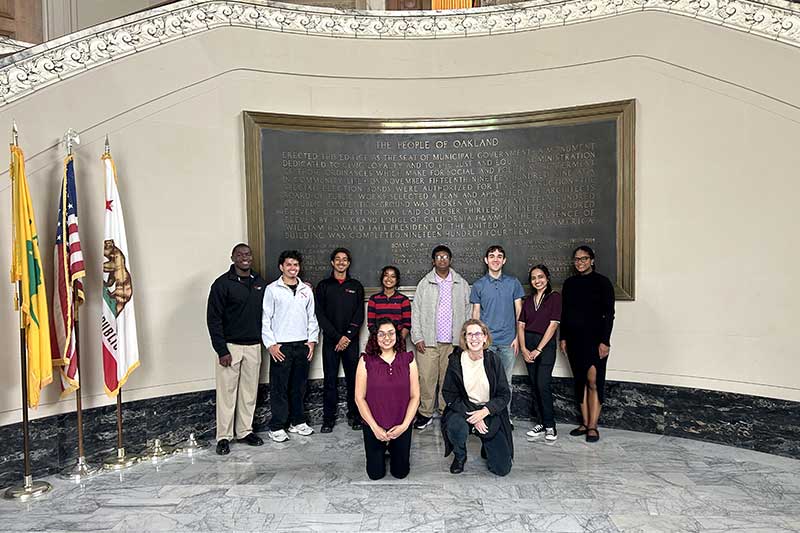 Khoury faculty and students smile in front of a large plaque in Oakland City Hall