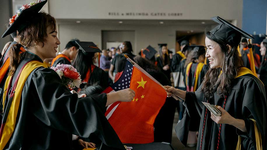 Class speaker Maizhou Yuan, left, talks with another graduate who is holding American and Chinese flags
