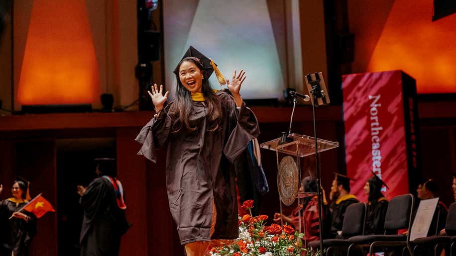 A graduate crosses the stage with her hands raised in celebration
