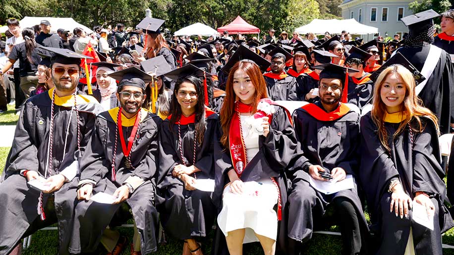 Six Khoury graduates sit in a row in a section of dozens of other graduates