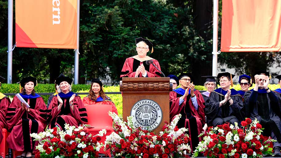 Oakland Dean Dan Sachs, who told attendees the day was in celebration of “one ceremony, two campuses, one Northeastern family,” is joined by faculty including Khoury Dean Beth Mynatt (seated second from right, first row)
