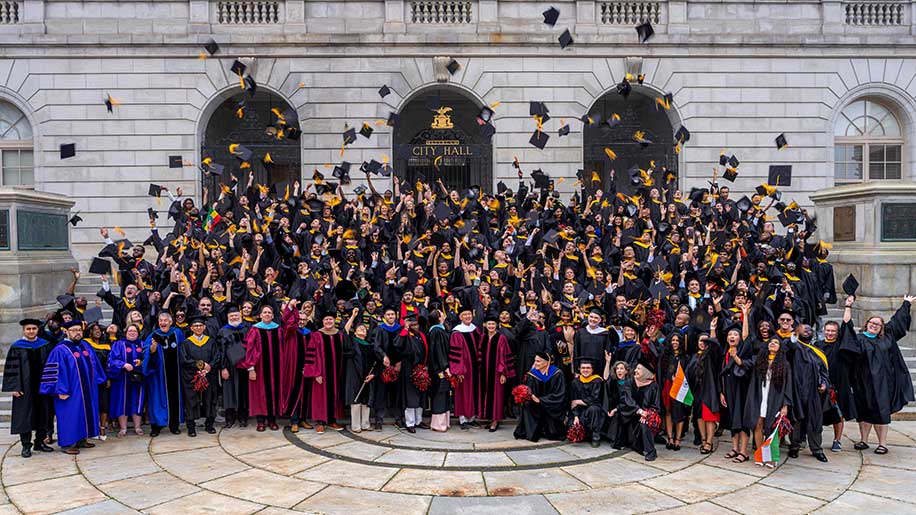 Hundreds of graduating students toss their caps in the air on the steps of Merrill Auditorium