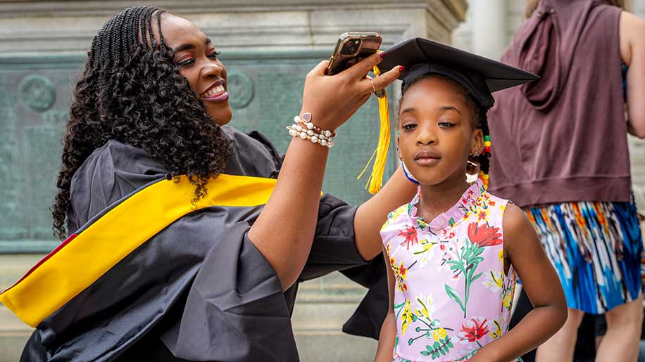 A Roux graduate places her graduation cap on a young girl outside the auditorium