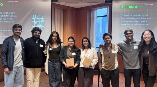 8 members of the Khoury Master's Students Council pose for a photo in front of two large presentation screens