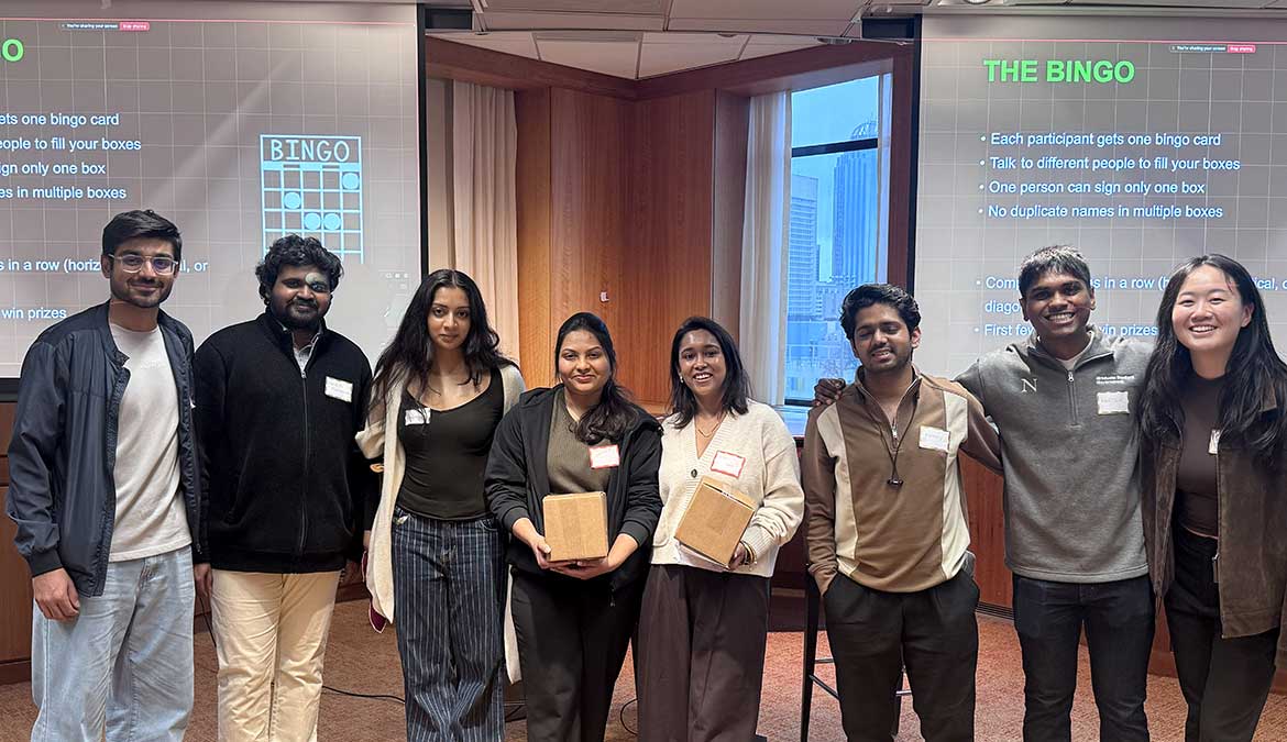 8 members of the Khoury Master's Students Council pose for a photo in front of two large presentation screens