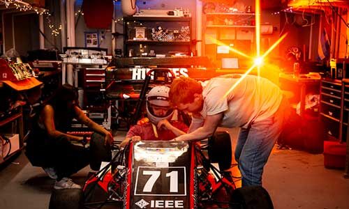 A student sits in a Northeastern Electric Racing team vehicle while two other club members examine the vehicle