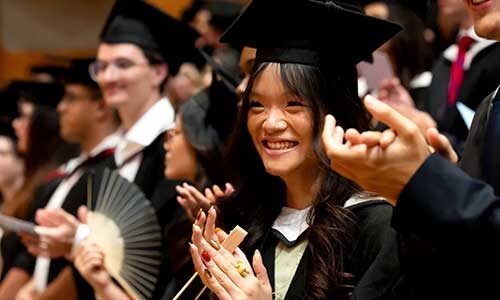 Several Northeastern University London students stand up and clap during the graduation ceremony