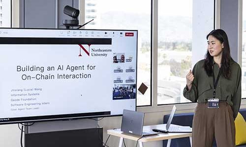 Jinxiang (Lucia) Wang stands next to a screen showing a presentation slide titled, "Building an AI Agent for On-Chain Interaction"