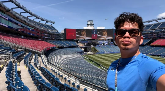 A young man taking a selfie against the backdrop of a large sports arena during the World Cup