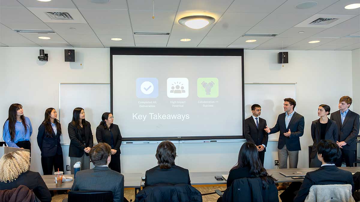 A group of eight Khoury students stand in front of a presentation screen showing a slide titled, "Key Takeaways"