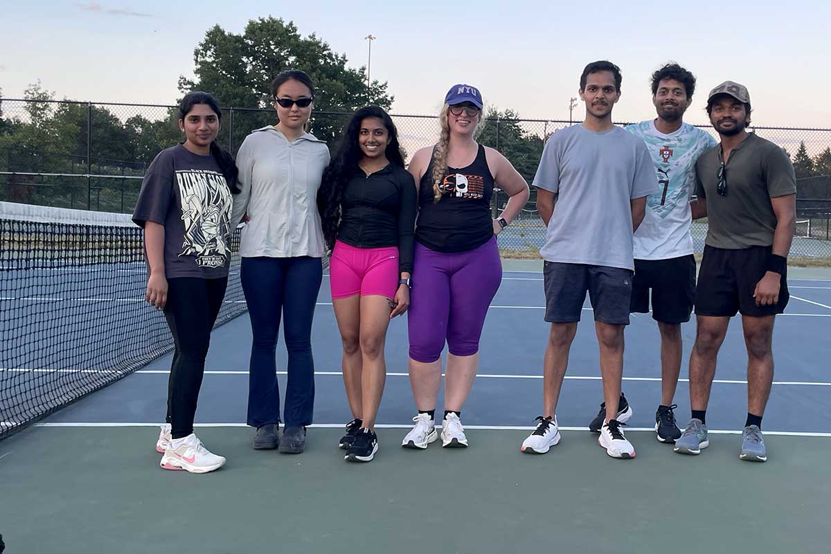 Seven members of the Roux tennis club pose for a photo on a tennis court next to the court's net