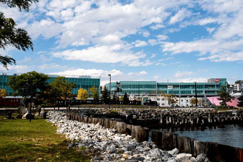 The exterior of the Roux Institute campus building shown with a harbor visible in the foreground