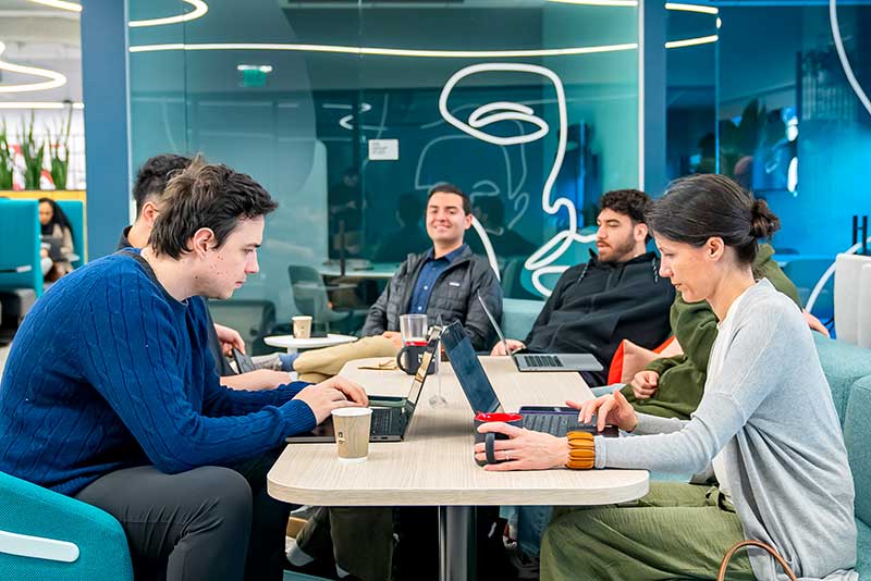 Six Khoury students sit around a large table working on their laptops at Northeastern University Miami
