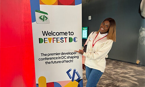 student Oluwatobiloba Mercy Akinwunmi next to a colorful Devfest DC sign