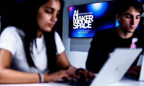 Two students work on laptops in Snell Library's AI Makerspace