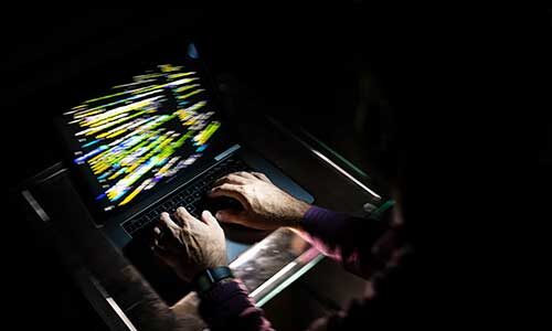 A person types on a laptop keyboard in a dark room