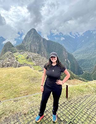 A student poses for a photo with mountain peaks and clouds in the background